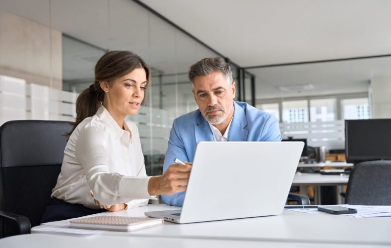 Two busy executive team business people working on computer at office meeting. Two busy professional executive team business people working together on business finances analysis looking at computer at office meeting. Professional manager consulting corporate client using laptop